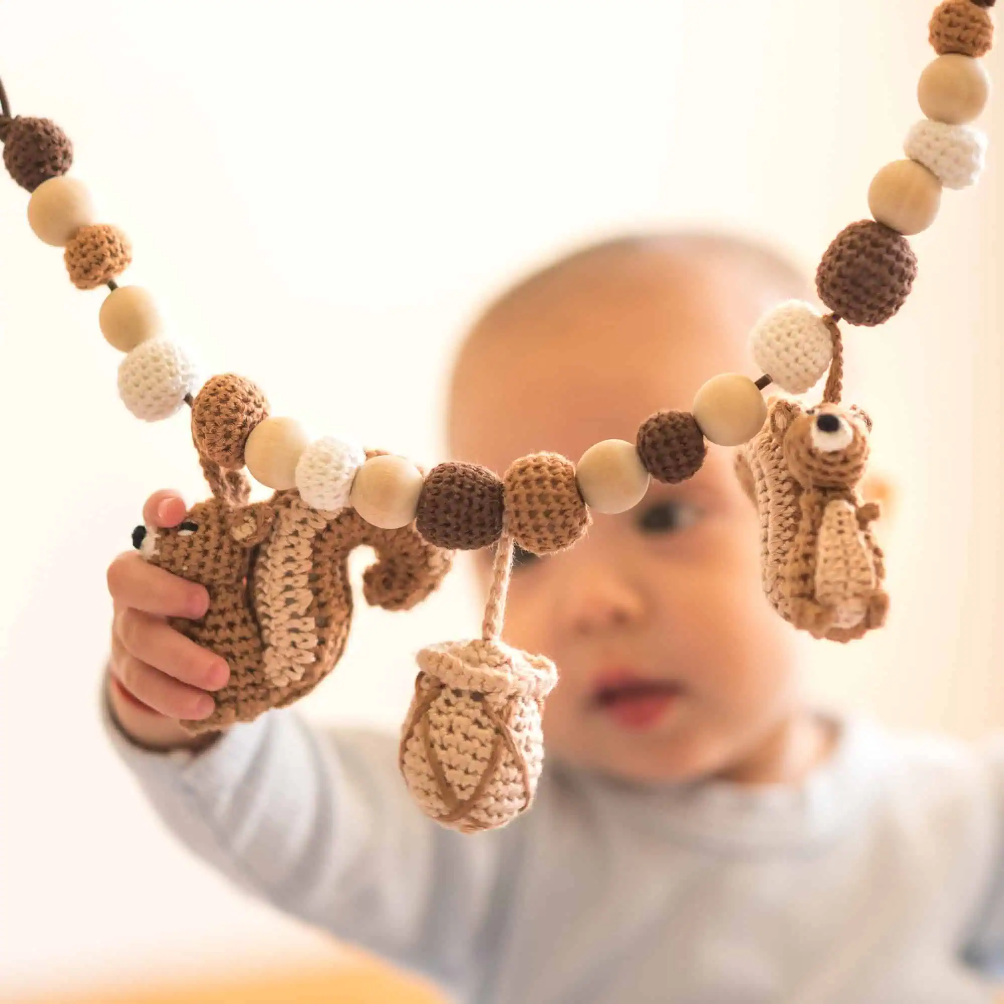 Baby greift von unten nach dem gehäkelten Eichhörnchen der Kinderwagenkette.