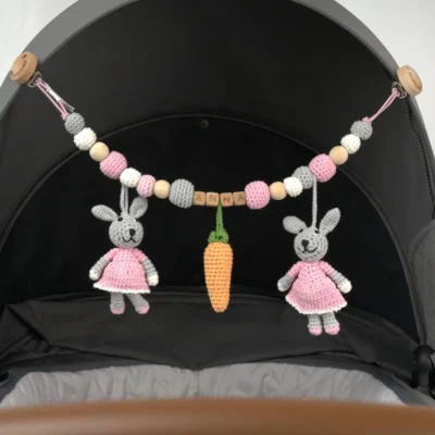 Personalisierte Kinderwagenkette mit Hase-Motiv und Namen Anna am Kinderwagen befestigt.