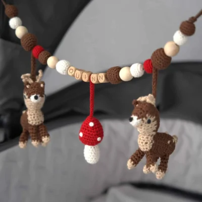 Personalisierte Kinderwagenkette mit Reh-Motiv und Namen Quinn am Kinderwagen befestigt.