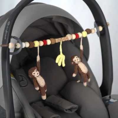 Personalisierte Kinderwagenkette mit Affe-Motiv und Namen Juna an der Babyschale befestigt.