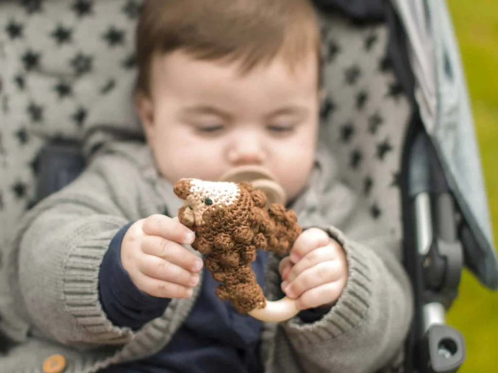 Baby hält eine Ringrassel mit Igel-Motiv und Holzring im Kinderwagen.